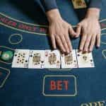 Five playing cards laid out on gaming table with hands touching a King and an Ace.