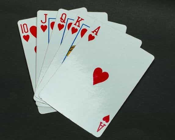 Five playing cards in the same suit of hearts lying flat on a grey surface.