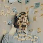 A man leaning against a wall, both of which are covered in dozens of post-it notes with various life affirmations and motivational slogans.