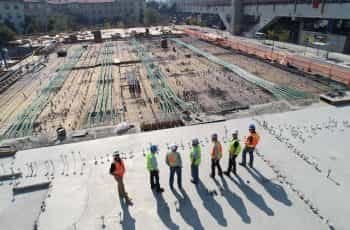 Seven workers or surveyors in high-vis and protective gear standing in a construction site and assessing the project’s progress.